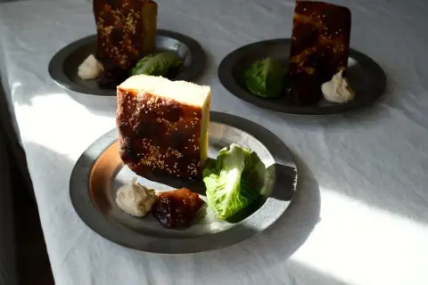 Enkel lyxig middag: bitar av rostat bröd med sesamfrön, serverade med sallad, en klick krämig röra och sylt på metalltallrikar.