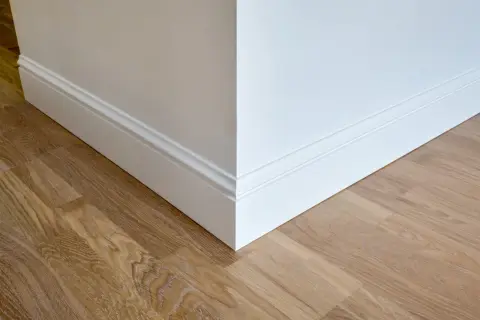 Coin de mur blanc avec plinthe moulurée et parquet en bois clair. La hauteur de la plinthe carrelage est bien visible.