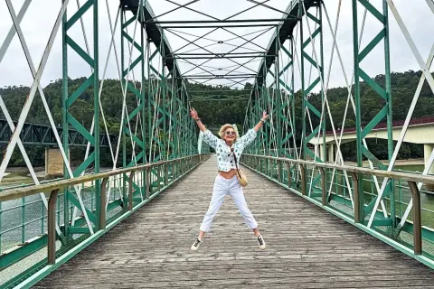 Mujer salta de alegría en un puente verde, disfrutando de las vistas. ¡Un lugar genial que ver en O Vicedo!