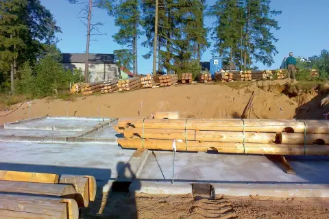 Drewniane bale przygotowane do budowy domu na betonowym fundamencie.