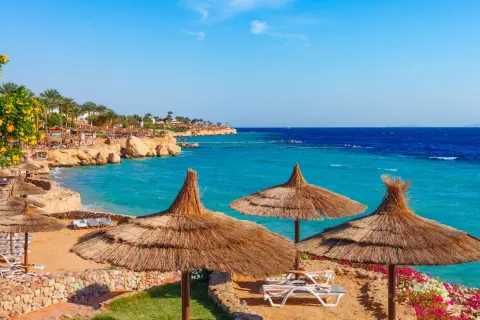 Słoneczna plaża w Sharm el Sheikh, z turkusowym morzem i leżakami pod strzechą. Idealne miejsce na wakacje, gdzie wiza otwiera drzwi do raju.