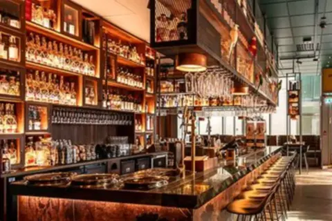 En elegant bar i Rom med hyllor fyllda med flaskor, en lång bardisk med stolar och hängande glas.