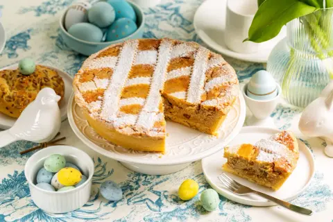 Une délicieuse pastiera napoletana saupoudrée de sucre glace, entourée d'œufs de Pâques colorés et d'une décoration printanière.