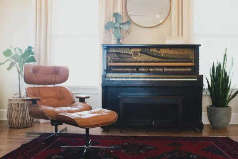 A brown leather armchair and ottoman, a mismatched pair, sit on a Persian rug next to an antique piano.