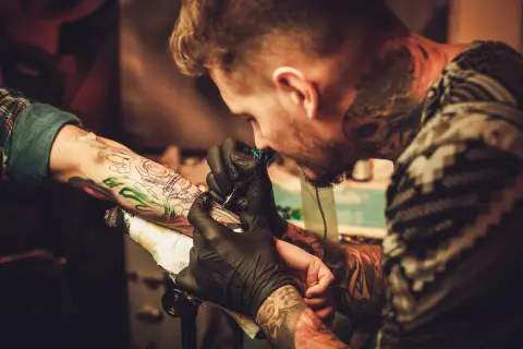 Tatuador con guantes negros trabaja en un brazo, creando un diseño detallado. Las opiniones de la Manuela Tattoo son muy positivas.