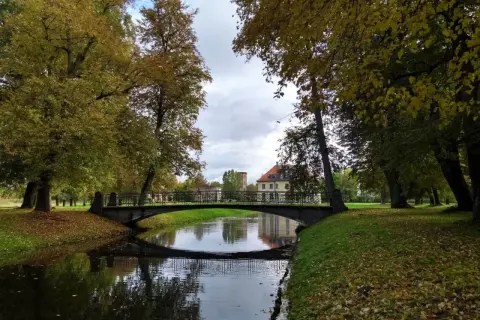 Jesienny park w Choroszczy z mostkiem nad kanałem i pałacem w tle.