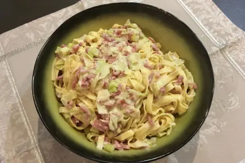 Un plat de tagliatelle poireaux crémeuses avec des lardons, servi dans un bol vert.