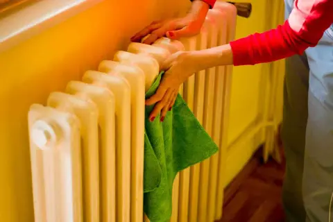 Mani che puliscono un termosifone in ghisa con un panno verde. Il lavaggio interno termosifoni in ghisa è importante per l'efficienza.