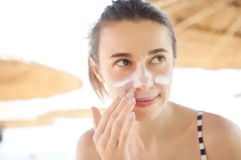 Frau trägt Sonnencreme auf ihr Gesicht auf, um Sonnenbrand zu vermeiden.