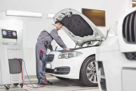 Mechanik sprawdza silnik białego BMW. Zastanawiasz się, ile teraz kosztuje przegląd samochodu?