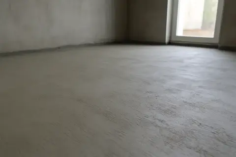 Świeżo wylana posadzka betonowa w pustym pomieszczeniu. Czekamy, aż beton wyschnie, zanim będziemy mogli kontynuować prace.