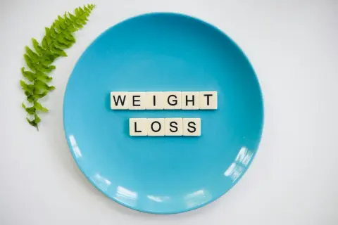 Niebieski talerz z literami "WEIGHT LOSS" i gałązką paproci. Idealny do planowania diety 10 kg w 2 tygodnie jadłospis.