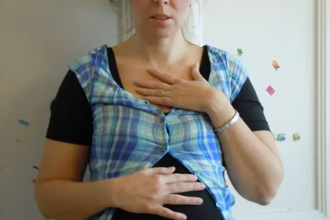 En kvinna med en rutig skjorta över en svart topp, håller händerna över magen. Hon ser ut att vara **rennie gravid**.