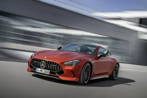 Pomarańczowy Mercedes-AMG GT 63 S pędzi po drodze, za nim rozmyte tło nowoczesnej architektury.