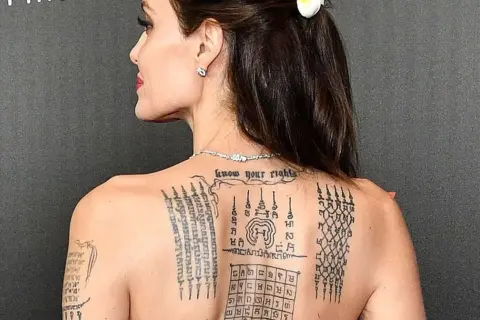 Angelina Jolie z tatuażem sak yant na plecach, przedstawiającym skomplikowane wzory i napisy.