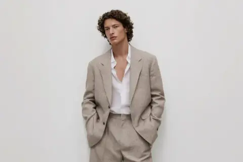 Uomo con giacca beige e camicia bianca sbottonata: un'idea di cosa mettere sotto la giacca uomo per un look casual-chic.