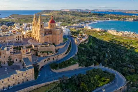 Malta, wyspa do kogo należy? Widok na kościół z czerwoną kopułą i kręte drogi na zielonym wzgórzu, z widokiem na morze i wybrzeże.