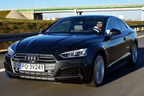 Czarny Audi A5 na drodze. Kierowca w okularach przeciwsłonecznych. Wiele osób chwali audi a5 opinie.