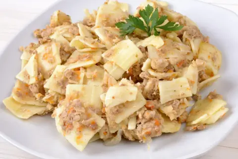 Pyszne lazanki z mielonym mięsem i warzywami, udekorowane gałązką natki pietruszki.