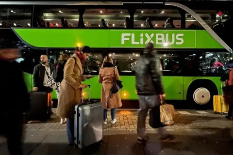 Ludzie z bagażem czekają na zielonego Flixbusa.