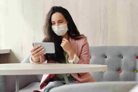Donna con mascherina guarda il telefono, forse per informarsi sulla situazione, mostrando una certa paura dei virus.