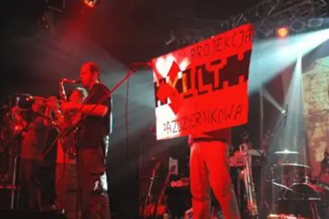 Koncert z instrumentami dętymi i banerem "PROJEKCJA KULTU PAZERMIKOWA". Koniec tekst.