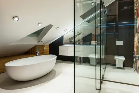 Élégante petite salle de bain mansardée avec baignoire îlot, douche vitrée, lavabo suspendu et WC.