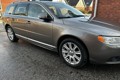 Grå Volvo V70 kombi, en pålitlig bil som kan behöva en ny motorlampa. Bilen står parkerad på en fuktig uppfart.
