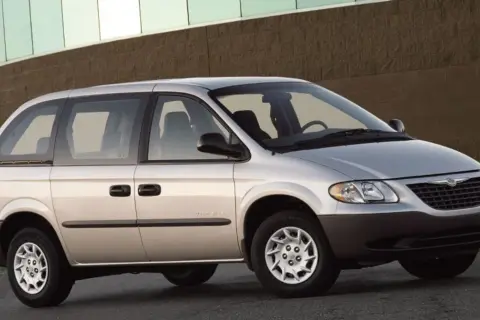 Srebrny Chrysler Voyager, gotowy na każdą podróż, zaparkowany przed budynkiem z ceglaną fasadą.