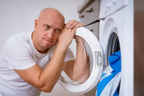Zmartwiony mężczyzna opiera głowę o otwarte drzwi pralki Whirlpool, która wyświetla błąd F05.