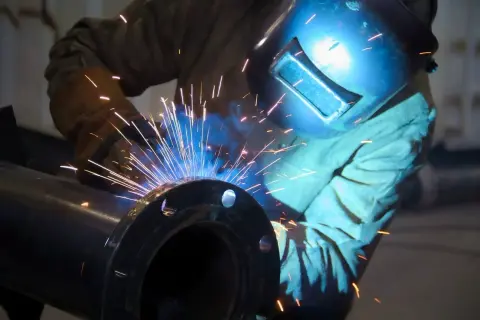 Spawanie żeliwa: iskry sypią się podczas precyzyjnej pracy spawacza w masce ochronnej, łączącego metalowe elementy.