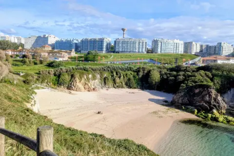 Playa en el parque de bens, con arena dorada, acantilados verdes y edificios modernos al fondo.