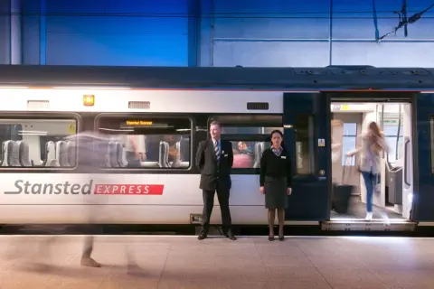 Pociąg Stansted Express na stacji. Pracownicy obsługi i pasażerowie wsiadają i wysiadają. Szybki transport z lotniska do centrum Londynu.