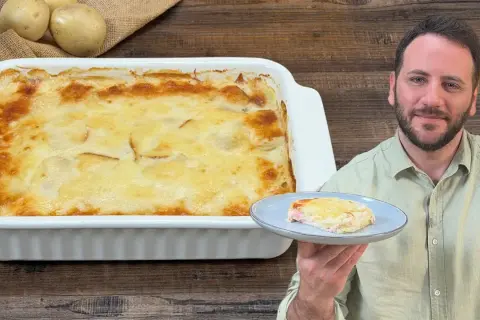 Un uomo sorride mostrando una porzione di parmigiana di patate appena sfornata, dorata e filante.