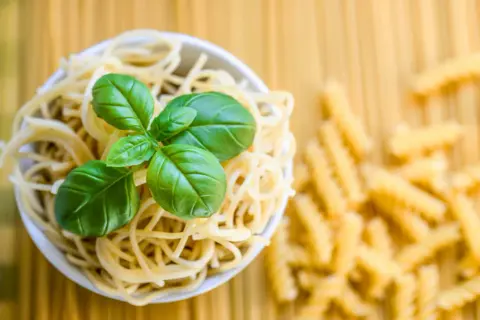 Miseczka spaghetti z bazylią, obok rozsypane fusilli. To klasyczne danie, gdzie co to jest semolina z pszenicy durum, stanowi podstawę.