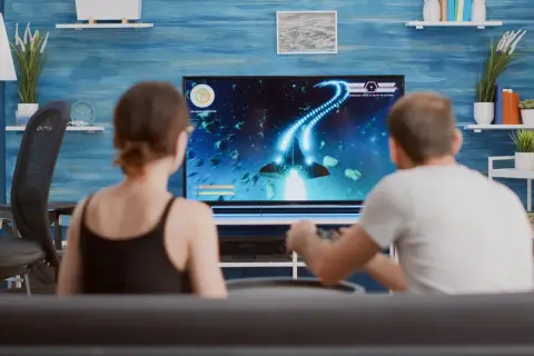 Para grająca w grę kosmiczną na dużym telewizorze.