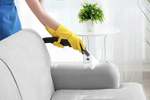 Person mit gelben Handschuhen reinigt Polstergarnitur mit einem Dampfreiniger.