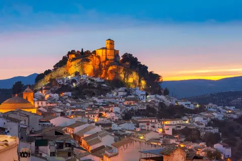 Pueblo blanco andaluz con castillo iluminado en la colina al atardecer. Un lugar encantador que ver cerca de Granada.