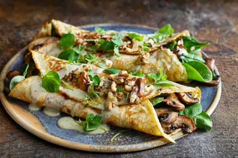 Herzhafte Pfannkuchen gefüllt mit Pilzen, garniert mit Nüssen und frischen Kräutern, übergossen mit cremiger Sauce.