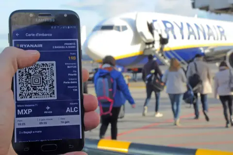 Telefon z kartą pokładową Ryanair, gotowy do podróży. W tle samolot i pasażerowie.