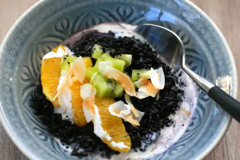 Schwarzer Reis mit Kokosmilch, garniert mit Orangenstücken, Kiwi und Kokoschips. Ein köstliches Dessert.