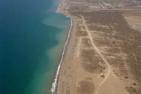 Vista aérea de la playa Torregarcia, con el mar turquesa a la izquierda y la costa arenosa con vegetación escasa y construcciones a la derecha.