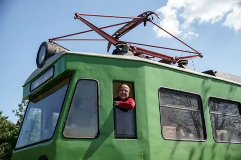 Uśmiechnięty maszynista w czerwonej bluzie wygląda z okna zielonego tramwaju, który kiedyś jeździł na trasie Łódź-Skierniewice.