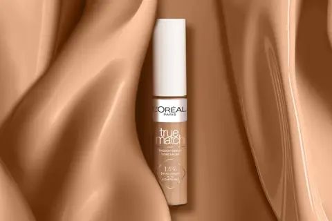Un correcteur jaune L'Oréal True Match, présenté sur un fond satiné couleur peau.