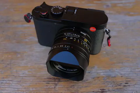 Leica Q3 test : un appareil photo noir élégant avec un objectif Summilux sur fond de bois.