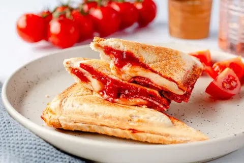 Herzhafte Sandwichmaker Rezepte: goldbraune Sandwiches mit geschmolzenem Käse und Tomatensoße, serviert mit frischen Tomaten.