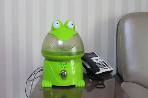 Zielony nawilżacz powietrza dla niemowlaka w kształcie żaby, obok telefonu.