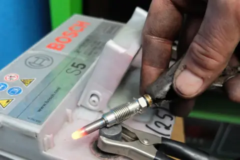Ręka mechanika testuje rozgrzany przekaznik świec żarowych podłączony do akumulatora Bosch S5.