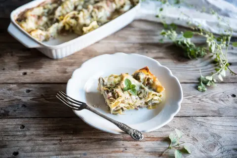 Una fetta di lasagne con carciofi surgelati, guarnita con menta, su un piatto bianco, accanto a una forchetta.
