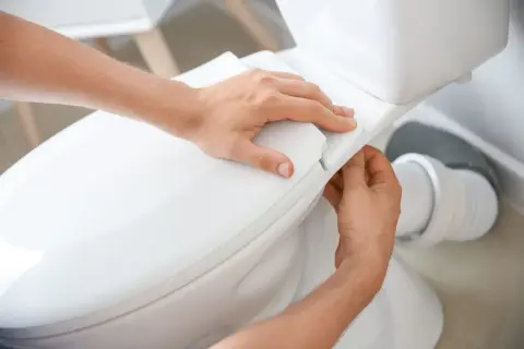 Mains ajustant le siège d'un WC. La hauteur de l'alimentation en eau du WC est correcte.